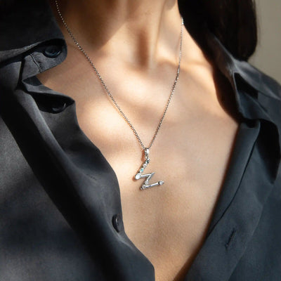 A person wearing a black shirt with an unbuttoned collar, showcasing the Awe Inspired Silver Gemstone Initial Necklace adorned with initial charms and a letter "Z" pendant.