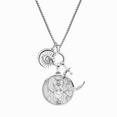 The Awe Inspired "Dancing in the Moonlight Charm Necklace" features a silver chain adorned with three exquisite charms: an intricate Hecate Pendant depicting a figure holding a staff and shield, a round pendant showcasing an eye and sun design, and a crescent moon embellished with a small gemstone.