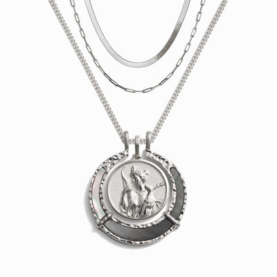 The Hunter's Moon Halo Necklace Set by Awe Inspired is a stunning silver necklace with three chains, featuring a prominent Artemis pendant that showcases an intricate relief of a person on horseback framed decoratively. This exquisite piece is crafted to absorb negative energy and impart an aura of protection to its wearer.