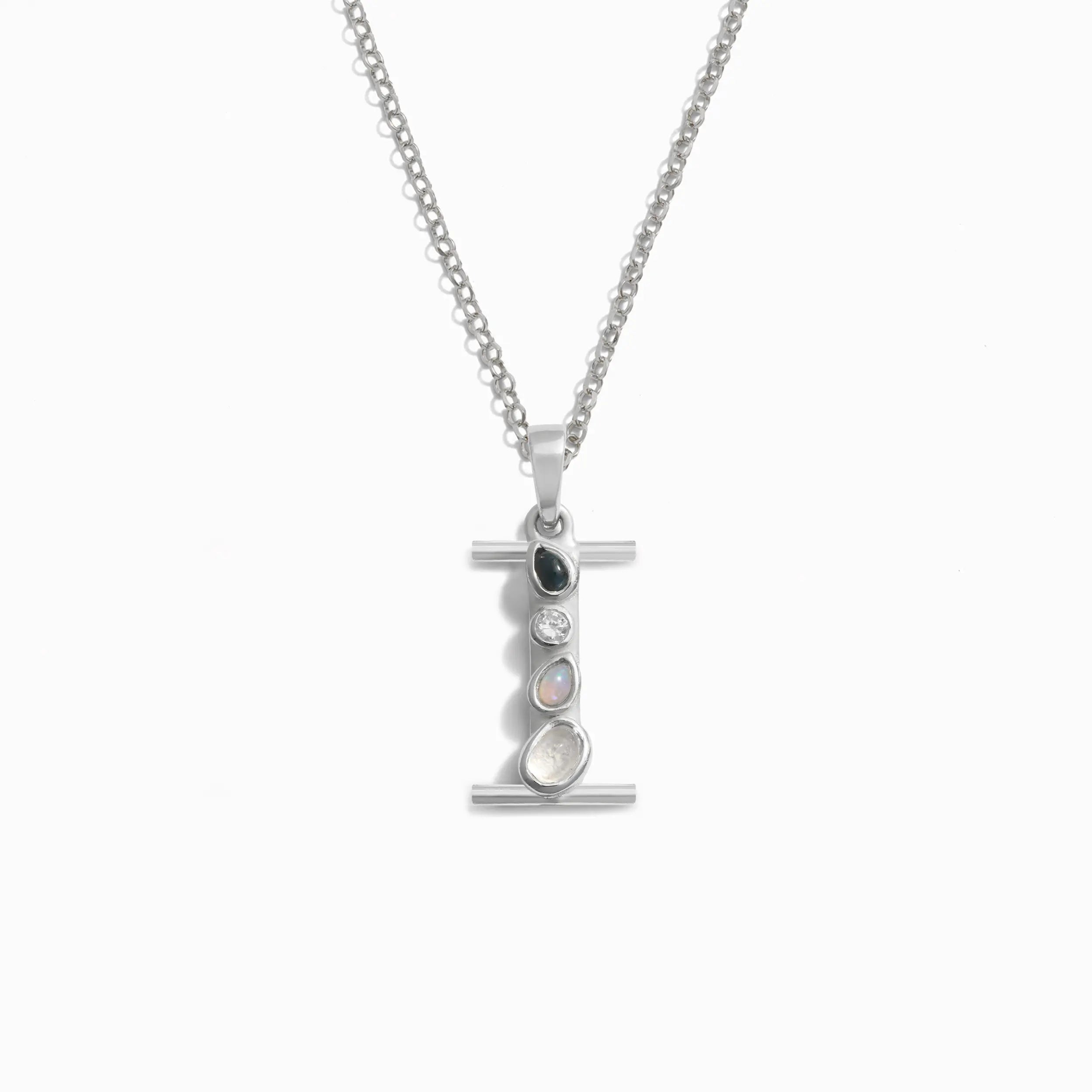 AWE Inspired presents the Silver Gemstone Initial Necklace, a statement-sized silver pendant necklace featuring a vertical bar adorned with four bezel-set gemstones in various shapes and colors, hanging from a fine chain.