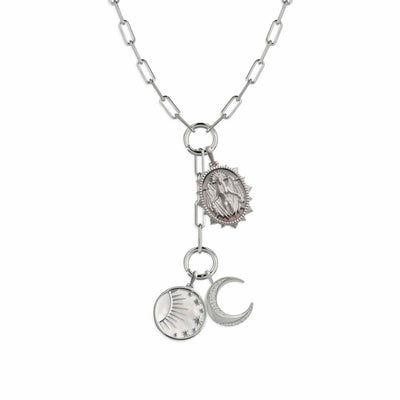 The Lilith Moon Lariat Charm Necklace by Awe Inspired features a silver chain adorned with multiple charm links, including a detailed oval medallion, a round pendant with a sun motif, and a crescent moon pendant suggesting the dark side of the moon.