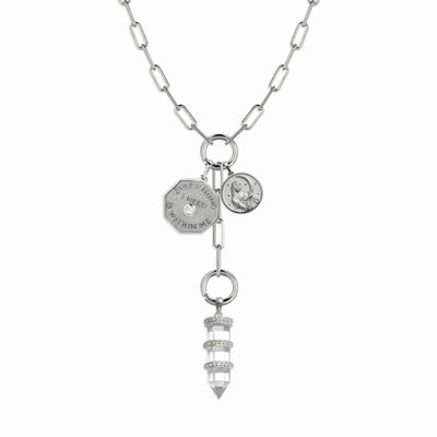 The Manifestation Charm Lariat by Awe Inspired features a silver chain necklace adorned with two coin-like pendants inscribed with "Everything I Need Is Within Me" and a crystal pendant wrapped in metallic bands.