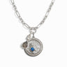 The Mother Earth Charm Necklace by Awe Inspired is a silver chain necklace adorned with an intricate pendant design, featuring gemstones including a teardrop-shaped gem, a small pearl, and a circular charm with a blue opal at the center.