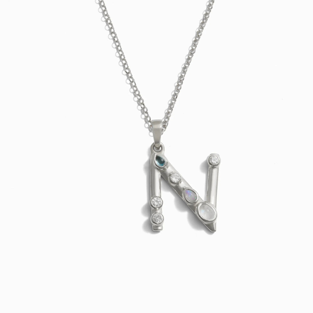 The Silver Gemstone Initial Necklace by Awe Inspired is a beautiful silver necklace featuring a statement-sized pendant shaped like the letter "N" and adorned with bezel-set gemstones.