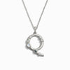 The Silver Gemstone Initial Necklace from Awe Inspired is a silver necklace featuring a statement-size circular pendant adorned with bezel-set gemstones arranged on one side.