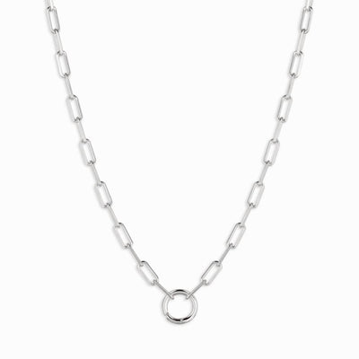 The Charm Collector Necklace by Awe Inspired features a silver chain with rectangular links, reminiscent of a paperclip necklace, and showcases awe charms with a circular pendant in the center.