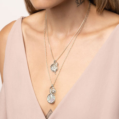 A person wearing the To The Moon And Back Necklace Set by Awe Inspired, dressed in a light pink top.