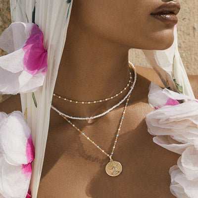 A woman wearing a white floral headscarf and a Trans Pride Beaded Enamel Necklace by Awe Inspired.