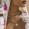 A woman wearing a white floral headscarf and a Trans Pride Beaded Enamel Necklace by Awe Inspired.
