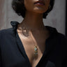 A person wearing a black shirt and the Peaceful Aura Charm Necklace by Awe Inspired, which features an intricate pendant design with dangling elements reminiscent of wind chimes.