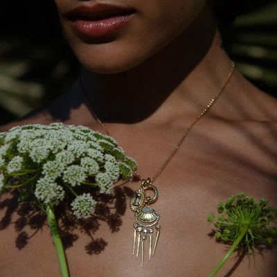 An individual wears the Peaceful Aura Charm Necklace by Awe Inspired, surrounded by white flowers, to balance their aura.