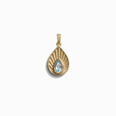 The Aura Pendant by Awe Inspired features a gold teardrop shape with a ridged design and a striking blue teardrop-shaped gemstone at its center, emanating an aura of elegance and balance.