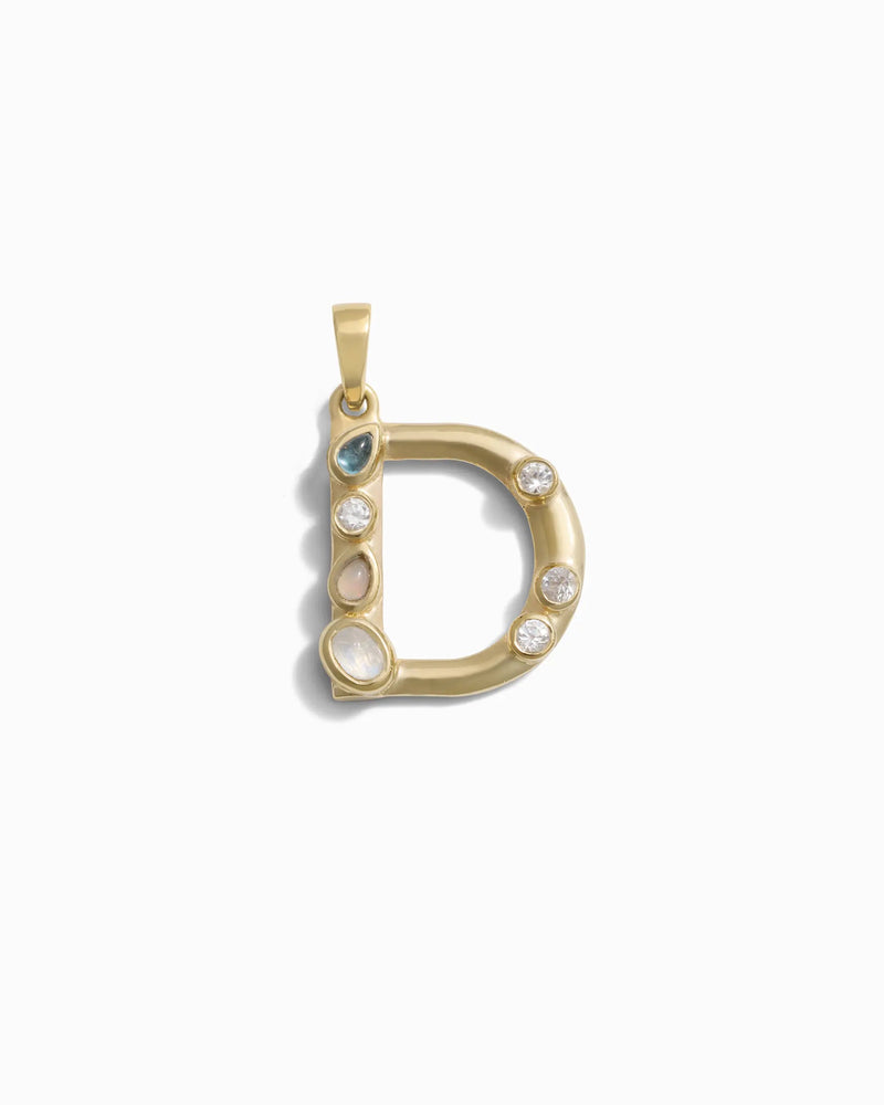 The Gemstone Initial Pendant by Awe Inspired is a gold pendant in the shape of the letter "D," featuring bezel-set gemstones, including diamonds and colored stones. This personalized jewelry piece makes a perfect addition to any collection, blending elegance with a touch of individuality.