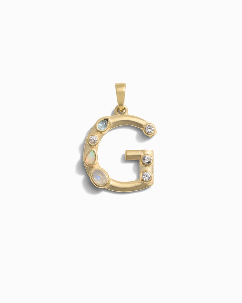 The Gemstone Initial Pendant by Awe Inspired is a gold pendant shaped like the letter "G," adorned with small round and oval bezel set gemstones, crafted as a unique piece of personalized jewelry.