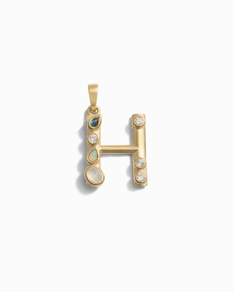 The Gemstone Initial Pendant by Awe Inspired, in the shape of the letter "H," is adorned with various bezel set gemstones including emeralds, opals, and diamonds—a perfect piece of personalized jewelry.