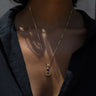 A person wearing the Awe Inspired Aura Pendant radiates an enigmatic aura. The gold necklace with a purple gemstone pendant rests elegantly against their black shirt, adding a touch of mystique to their appearance.