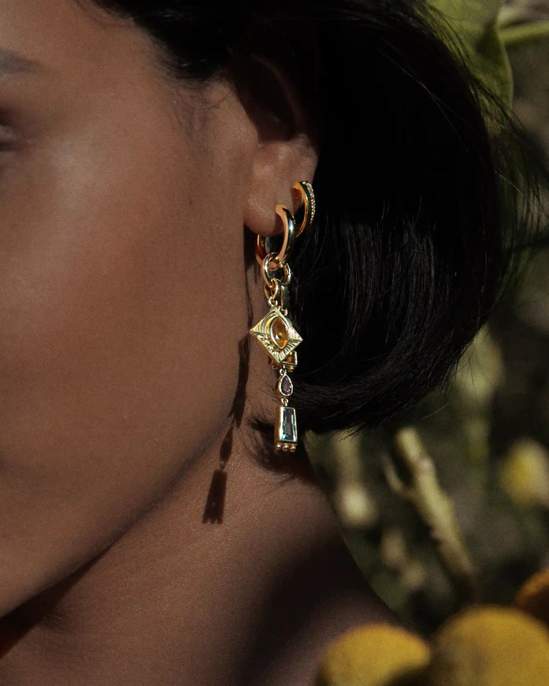Close-up of a person wearing the Awe Inspired 'Aura Pendant' earrings, featuring multiple geometric shapes, with a blurred natural background that enhances the aura.