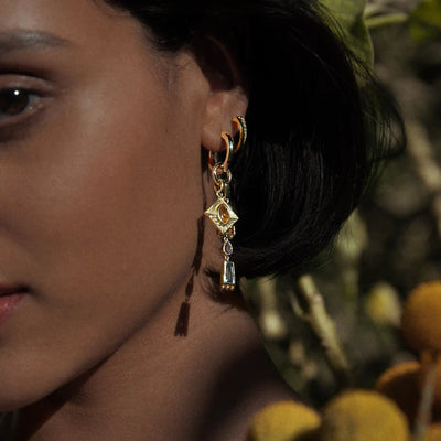 Close-up of a person wearing the Awe Inspired 'Aura Pendant' earrings, featuring multiple geometric shapes, with a blurred natural background that enhances the aura.