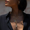 A person wearing a Gemstone Initial Pendant by Awe Inspired, along with multiple other pendants and personalized jewelry, paired with a dark, open-collared shirt.