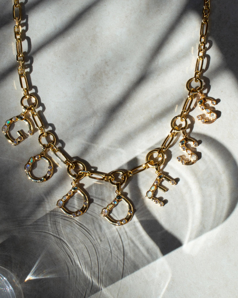 An Awe Inspired Gemstone Initial Pendant necklace with the word "GODDESS" spelled out in individual, jewel-encrusted letters, enhanced with bezel set gemstones.