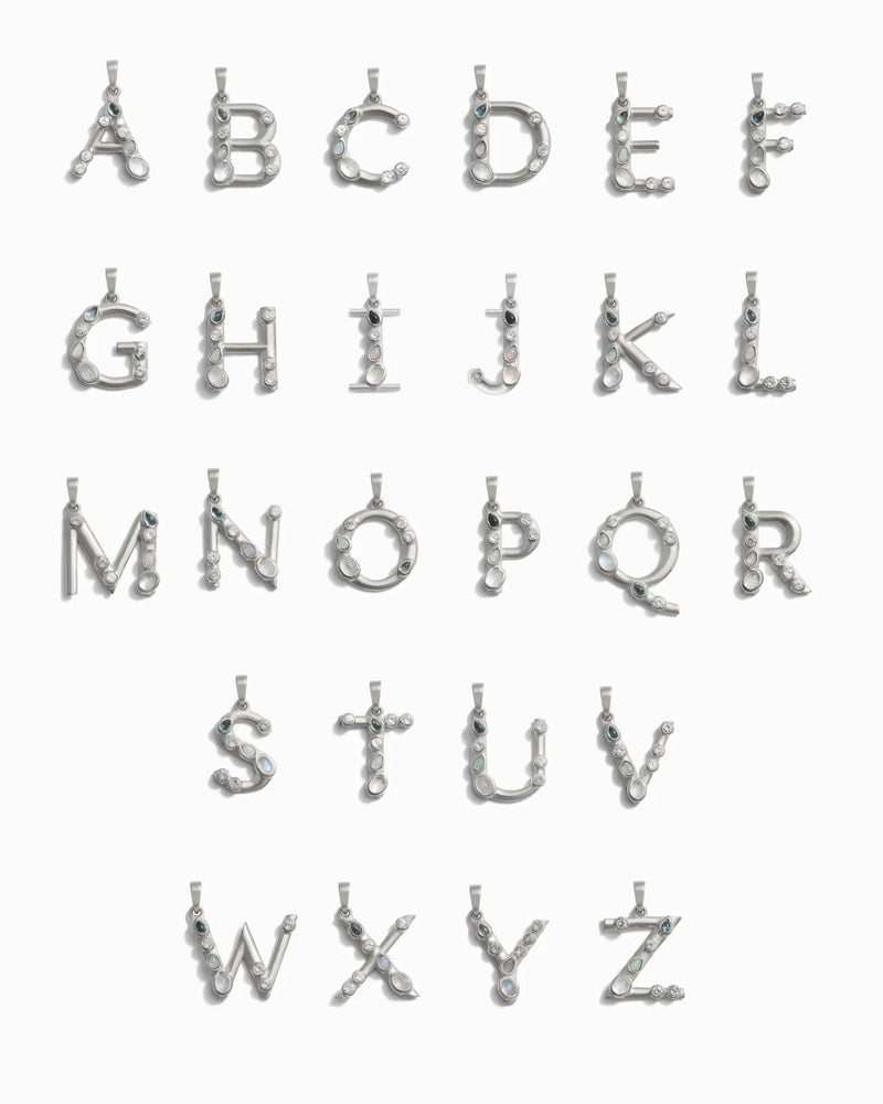 Introducing the Gemstone Initial Pendant by Awe Inspired—a collection of personalized jewelry featuring pendants shaped like the letters A to Z, each adorned with bezel-set gemstones or crystals.