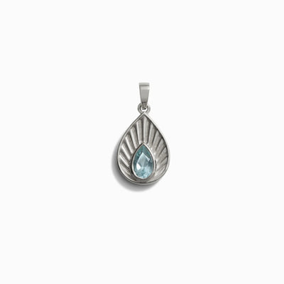 The Aura Pendant by Awe Inspired, featuring a blue gemstone set in a teardrop-shaped silver-toned setting, is showcased against a plain white background, radiating an aura of serene elegance.