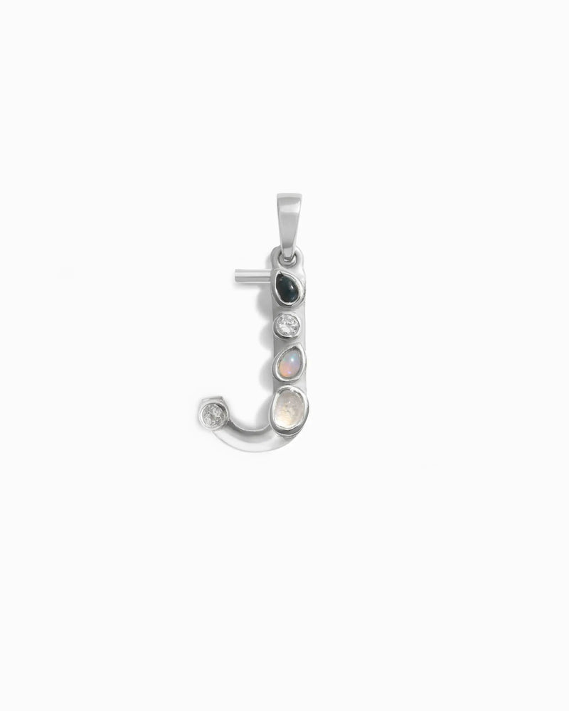 The Gemstone Initial Pendant by Awe Inspired is a silver pendant in the shape of the letter "J," adorned with five small, bezel-set gemstones in various colors.