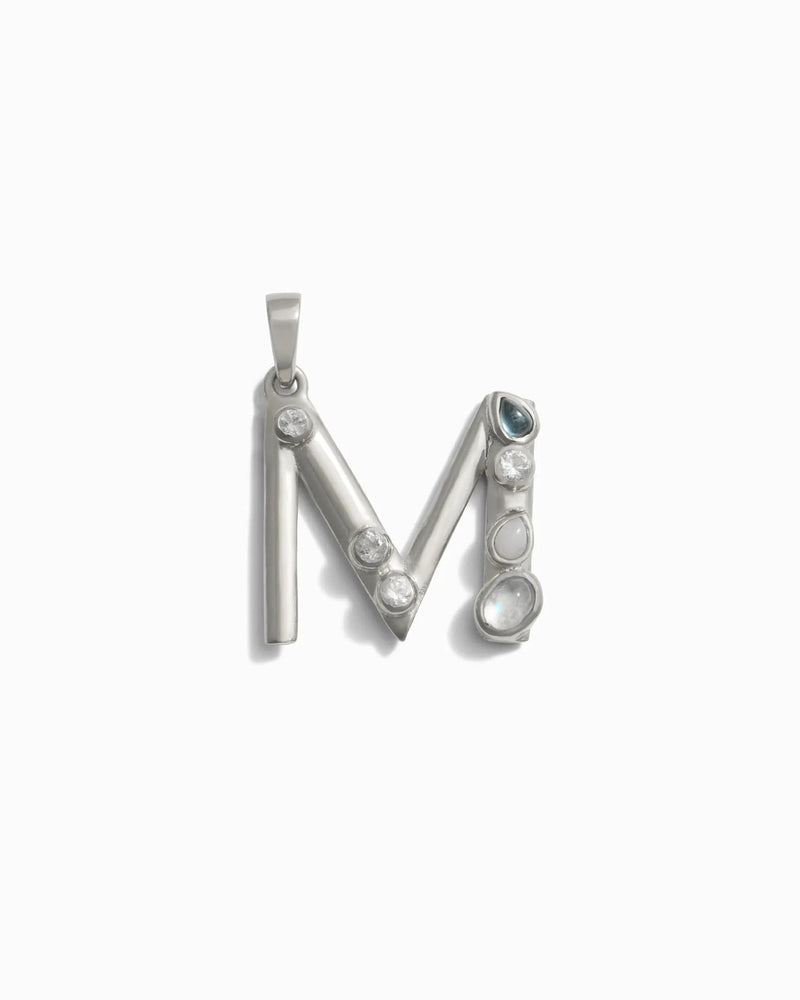 The Gemstone Initial Pendant by Awe Inspired is a stunning silver piece shaped like the letter "M," adorned with five bezel set gemstones of varying sizes and shapes, making it a perfect piece of personalized jewelry.
