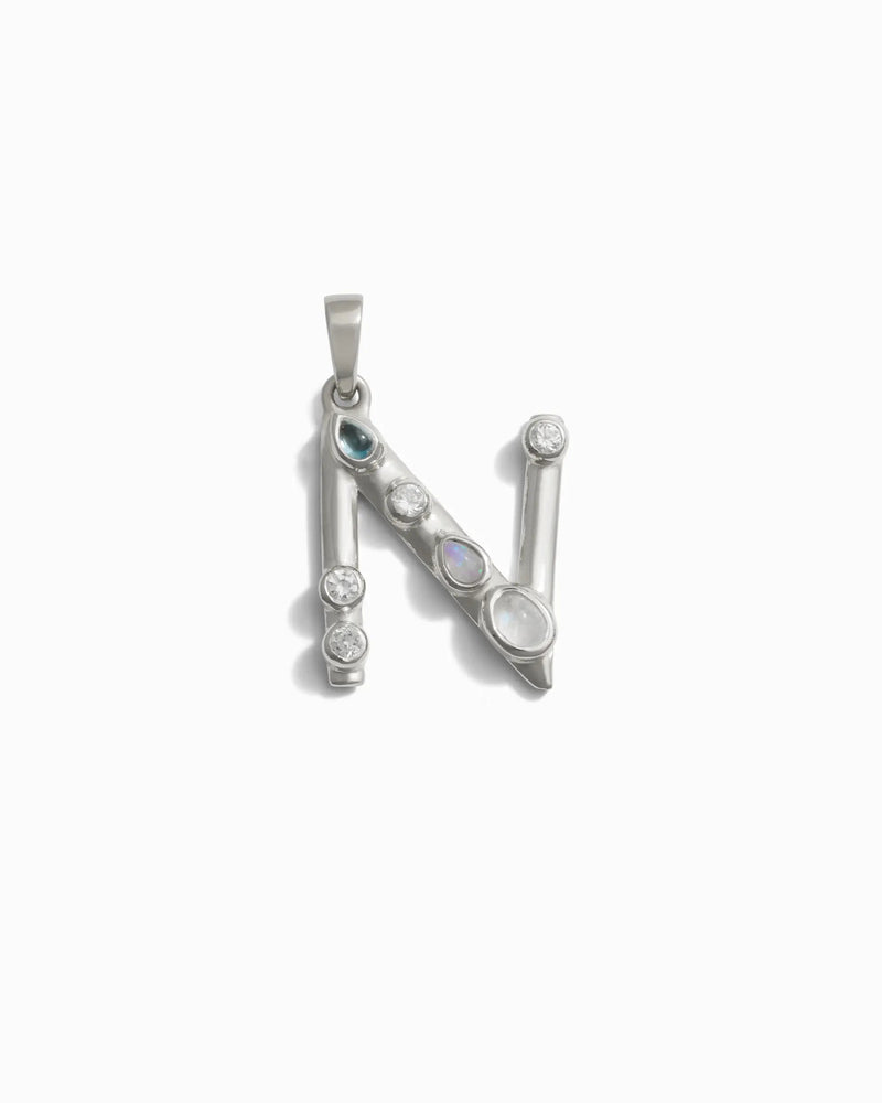 The Gemstone Initial Pendant by Awe Inspired is a silver pendant in the shape of the letter "N," adorned with multiple bezel set gemstones, creating a stunning piece of personalized jewelry.