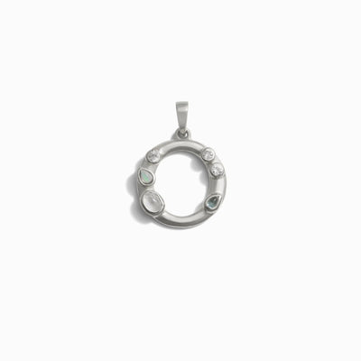 The Gemstone Initial Pendant by Awe Inspired is a circular silver pendant adorned with various bezel-set gemstones, including small circular and teardrop shapes, on a white background.