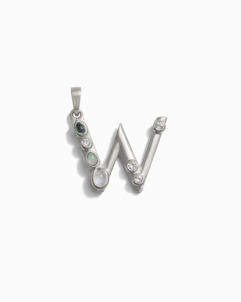 The Gemstone Initial Pendant by Awe Inspired is a silver pendant in the shape of the letter "W," adorned with bezel-set gemstones, including opals and what appear to be diamonds, set along its frame. This piece stands out as a personalized jewelry item perfect for those who love initial charms with a touch of elegance.