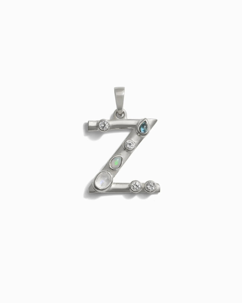 The Gemstone Initial Pendant from Awe Inspired is a stunning piece of personalized jewelry, featuring a silver pendant shaped like the letter 'Z' and adorned with bezel-set gemstones, including pearl and aquamarine.