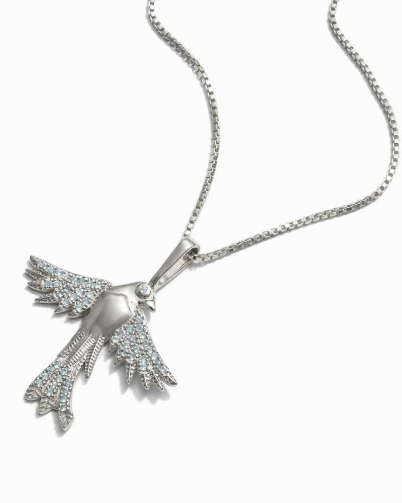 The Suffragist Bluebird Amulet by Awe Inspired features a bird-shaped pendant with light blue topaz gemstones, depicting a bluebird with wings spread, elegantly hanging from a chain-link necklace.