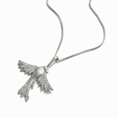 The Suffragist Bluebird Amulet by Awe Inspired features a bird-shaped pendant with light blue topaz gemstones, depicting a bluebird with wings spread, elegantly hanging from a chain-link necklace.