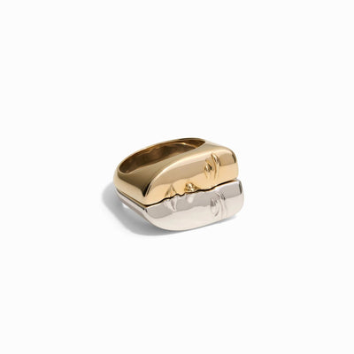 The Awe Inspired Face to Face Rings consist of two interlocking metallic nesting rings, one gold and one silver, showcased side by side on a white background. Each ring boasts a simple, smooth surface.