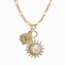 The True North Charm Necklace by Awe Inspired features a gold chain with large, interlocking oval links. It includes a Sun & Moon amulet adorned with gemstones and a compass pendant. The sun pendant has a mother-of-pearl center.