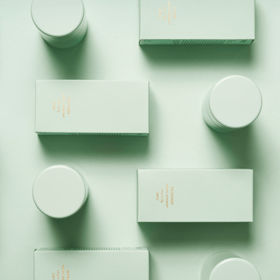 An arrangement of green rectangular boxes and cylindrical containers on a green background, showcasing Third Rose Deodorant, a long-lasting deodorant with a water-based formula by Corpus.