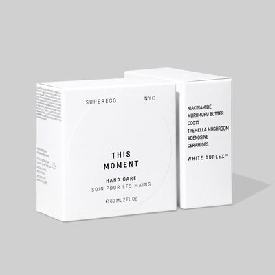 Two white boxes of This Moment Hand Care by Superegg, featuring ingredients like niacinamide, hyaluronic acid, and murumuru and shea butters, from Superegg, NYC, against a plain background.