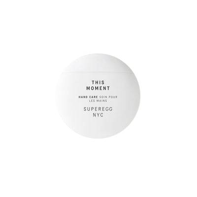 A round, white container labeled "This Moment Hand Care by Superegg," enriched with Niacinamide for enhanced skin nourishment.